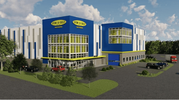 Modern storage facility with blue and white exterior, featuring large glass windows and multiple stories. Several cars are parked outside, and a delivery truck is visible in the parking lot.