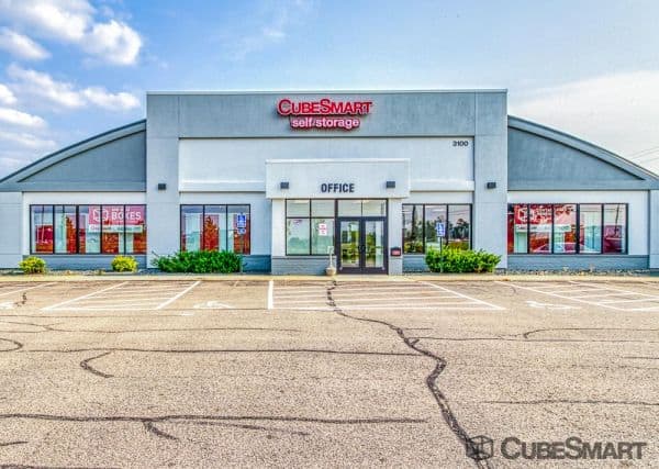 A CubeSmart self-storage facility, featuring a gray and white exterior with red signage, and an empty parking lot in front.