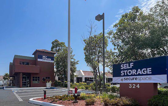 Self-storage facility with a brown building and blue signage, surrounded by trees and a parking area.