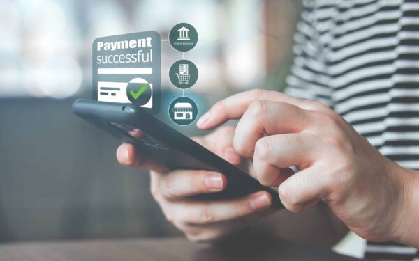 Person using a smartphone to make a payment. Display shows "Payment successful" with digital icons for online banking and shopping in the background.