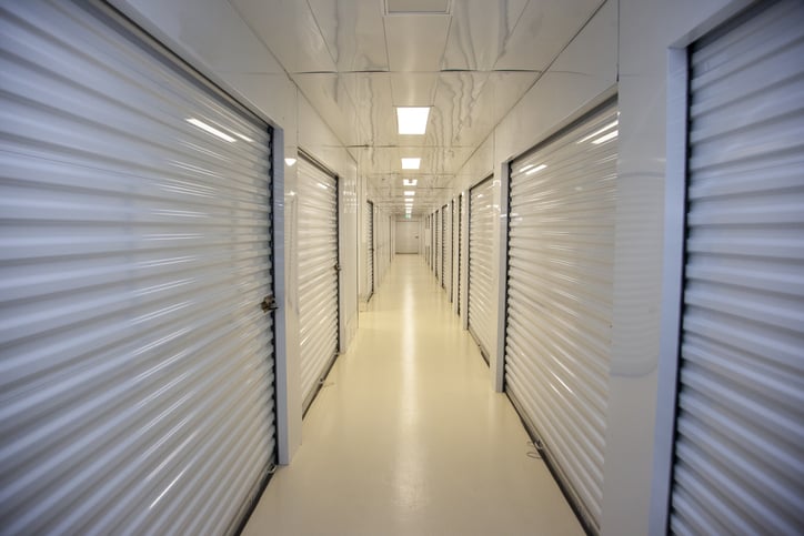 A corridor with white storage unit doors on both sides, bright overhead lighting, and a shiny beige floor.