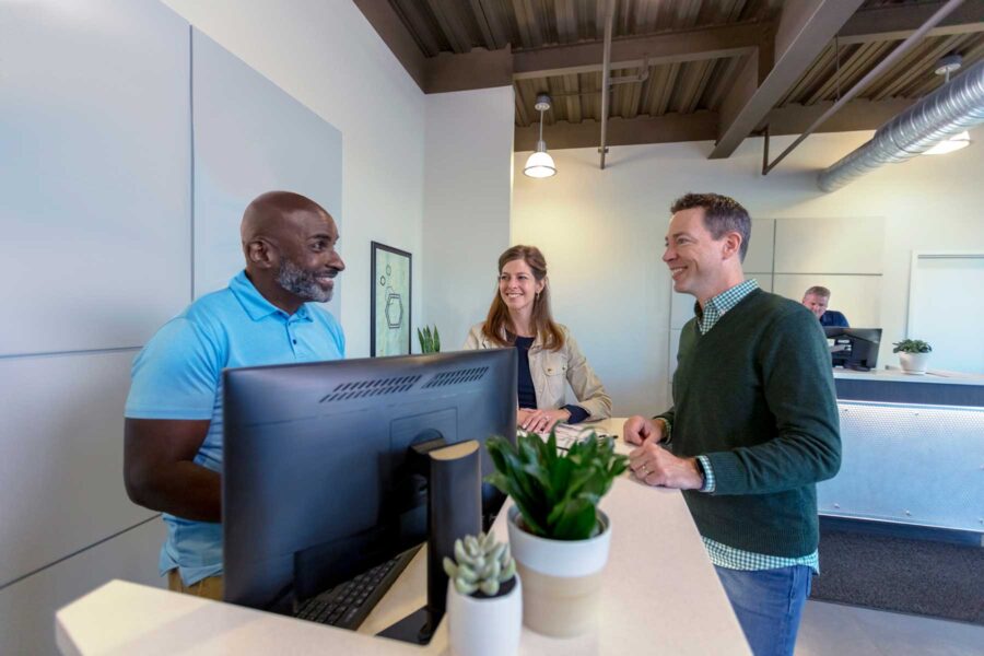 A man in a light blue polo is standing at a computer and helping two storage unit customers.
