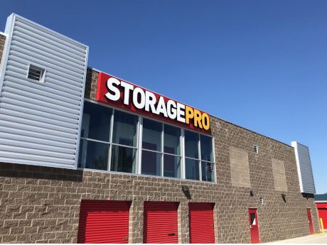 Storage facility with a "STORAGE PRO" sign, featuring red doors and a brown brick facade under a clear blue sky.