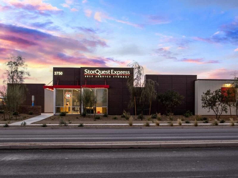 Modern storage facility with "StorQuest Express" signage, located at 3750, featuring a landscaped entrance, set against a colorful sunset sky.