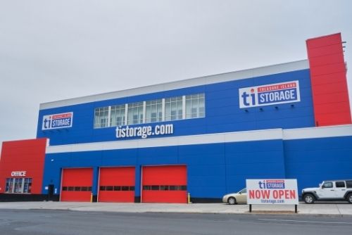 Bright blue and red self-storage facility with "ti storage" branding. Large sign in front reads "NOW OPEN.