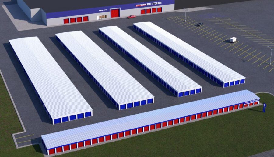 Aerial view of a self-storage facility with multiple long white-roofed storage units and a main building in the background. Some cars are in the parking lot.