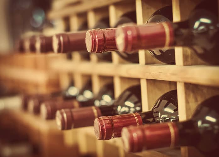 Rows of wine bottles stored horizontally in a wooden rack, with focus on the bottle necks and corks.