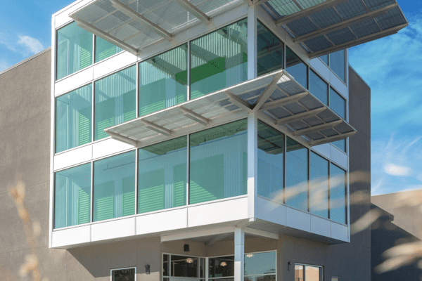Modern building with large glass windows and solar panels extended from the roof, set against a clear blue sky.
