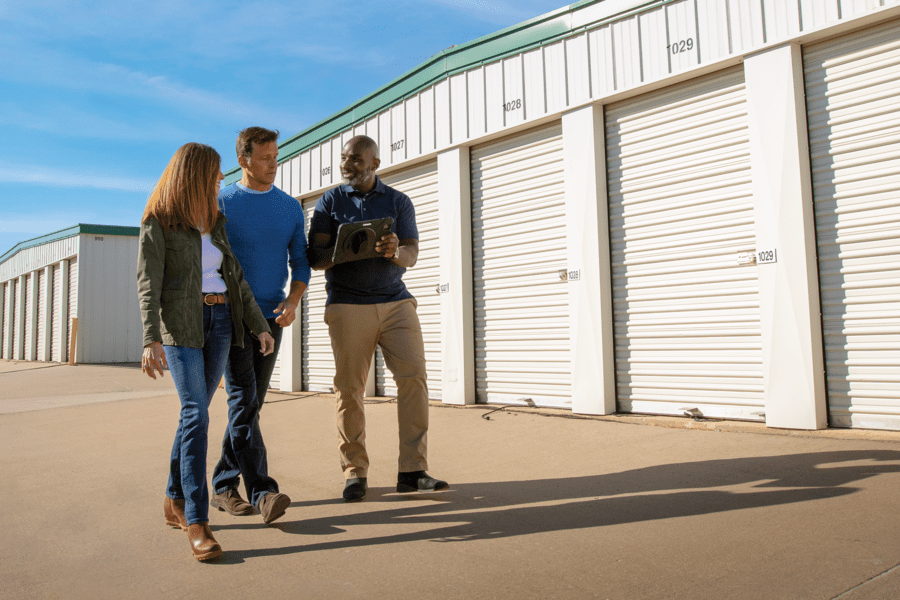 Three people stand outside storage units. One holds a clipboard.