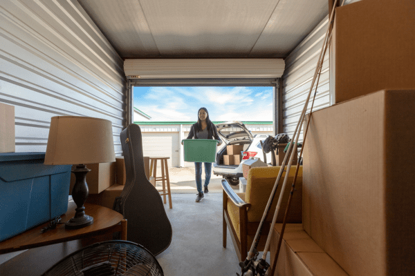 Tenant walking into a filled up storage unit with a box in her hands