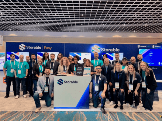 A group of people posing in front of a booth with "Storable" signs at a convention center, under a checkered ceiling.