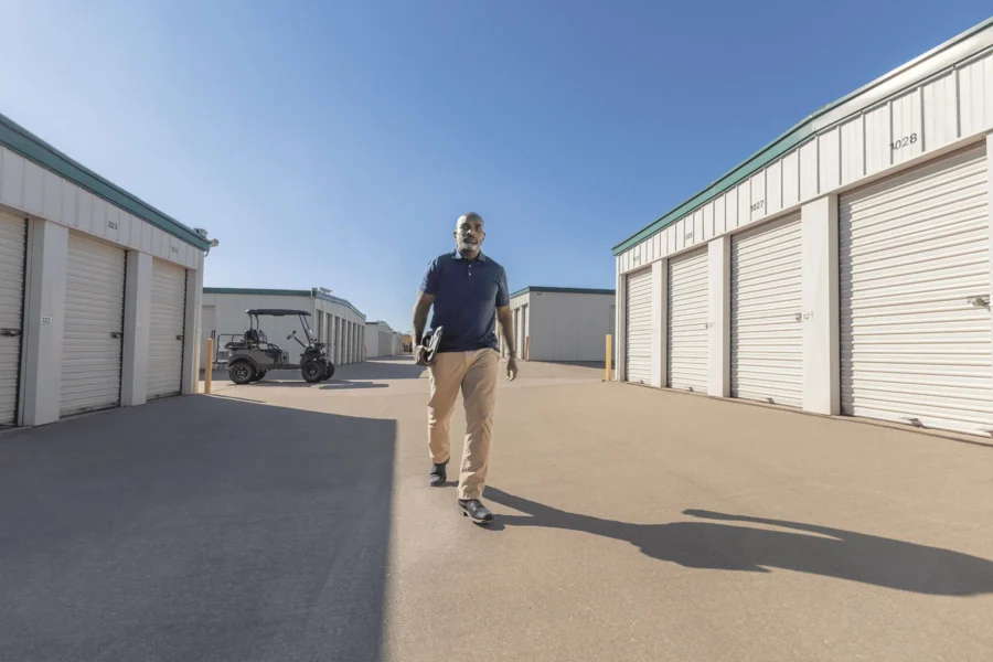 Man walking on a paved path between storage units under a clear blue sky, with a golf cart in the background.