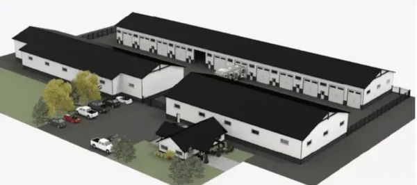 Aerial rendering of a facility with three long, white buildings with black roofs, a small entrance building, parking area with cars, and surrounding grass and trees.